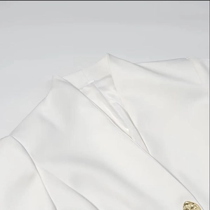 Détail du blazer blanc à col en V avec texture tissée et bouton doré élégant