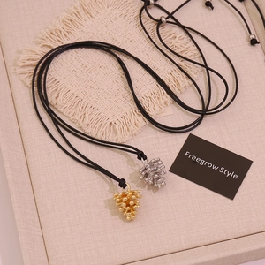 Creative gold and silver pinecone pendant necklaces with adjustable black cord on fabric