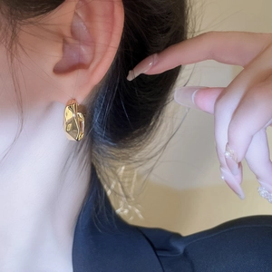 Close-up of golden geometric pleated earrings on model ear showing metallic texture