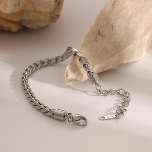 Macro view of silver stainless steel woven chain bracelet featuring a K18 engraved tag
