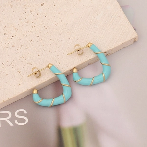 Detailed shot of light blue enamel C-shaped earrings with gold spiral accents on stone