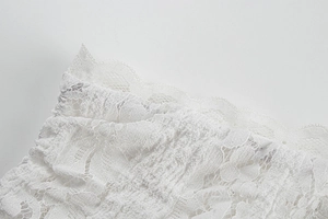 Close-up of fine white floral lace fabric with scalloped eyelash edge on dress