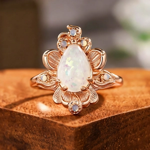 Vintage roségouden ring met peervormige opaal en bloembladpatronen op hout