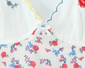 Close-up of white cotton dress featuring intricate red floral embroidery and wavy hem