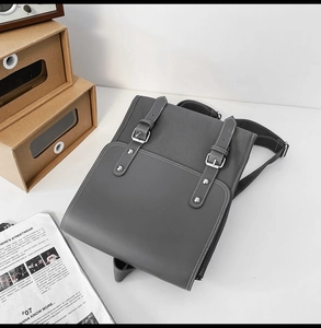 Top view of a grey faux leather backpack with silver buckles on a minimalist white desk