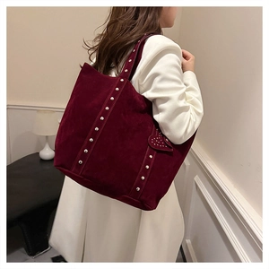 Detail of burgundy suede tote bag featuring metallic rivet studs and a heart ornament