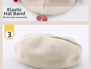 Detail of oat-colored knitted baby beret featuring elastic band and red cherry accents