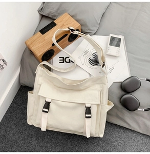 Sac à bandoulière en toile beige avec boucles noires posé sur un lit gris douillet