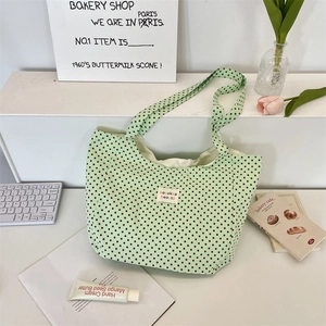Close-up of light green polka dot canvas tote bag with woven logo label in home setting