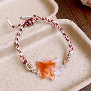 Makro-Detail des rot-weiß geflochtenen Armbands mit einem orangefarbenen Fuchshänger