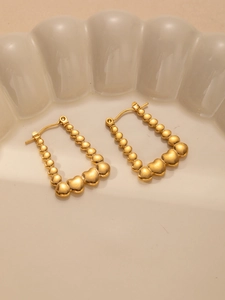 Detail of gold titanium steel heart earrings with textured bead pattern and U-shaped design