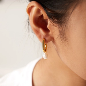 Elegant gold hoop earrings with natural freshwater pearl pendants on a female model