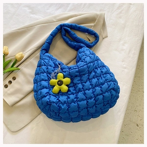 Close-up of blue quilted bubble tote bag with a yellow flower charm on a beige blazer