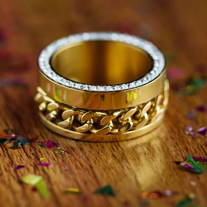 Luxury gold Cuban link chain ring with sparkling side-set crystals on dark wood base