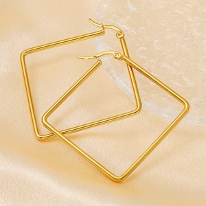 Macro view of gold-plated square hoop earrings on elegant silk and textured glass