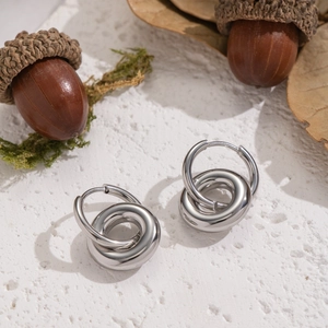 Silver interlocking double hoop earrings on a textured background with natural acorns