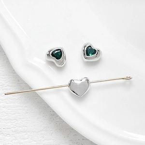 Macro detail of heart-shaped silver charms with emerald green zircon for DIY jewelry making
