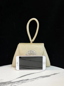 Detail der goldene Pailletten-Abendtasche mit Strassverschluss neben einem Smartphone