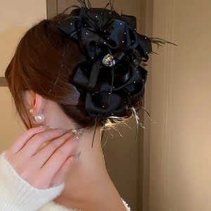 Détail d'une pince à cheveux en satin noir avec cristal coeur et plumes élégantes