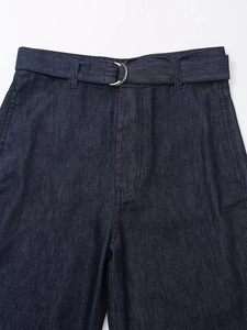 Détail d'un pantalon en denim indigo foncé à taille haute avec ceinture à boucle en D