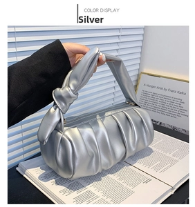 Close-up of silver pleated cylinder bag with knot handle and metallic faux leather texture