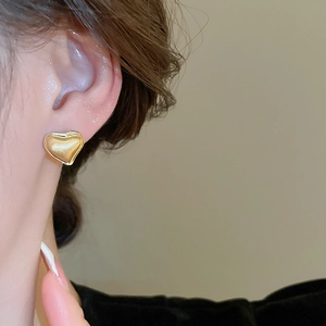 Detail of heart-shaped gold earrings with brushed finish and polished edges on a model