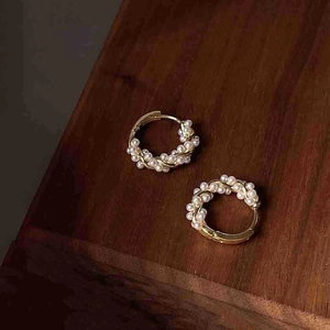 Detailed close-up of gold twisted hoop earrings with white pearls on a wood surface
