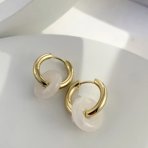 Detail view of gold stainless steel hoop earrings with white natural stone pendants