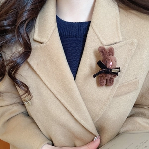 Detail of a brown fuzzy rabbit brooch with a black bow on a camel wool coat collar