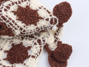 Close-up of v-neck knit vest featuring hollow-out crochet patterns and pom-pom details