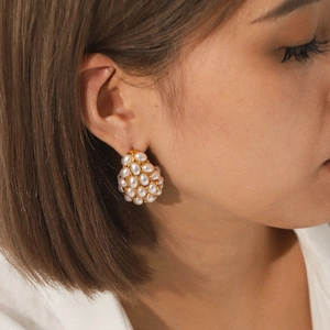 Close-up of golden teardrop earrings with clustered white pearls worn by a model