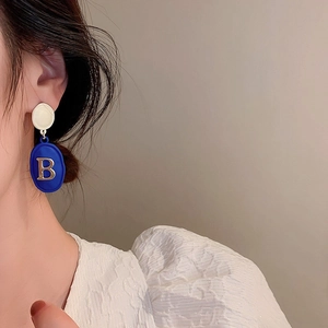 Detail view of Klein blue earrings with golden B letter worn by a female model