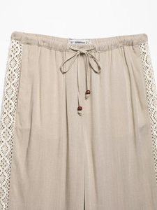 Detail showing elastic waistband with drawstring, wood beads, and lace trim on beige pants