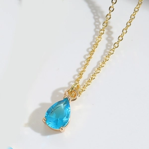 Macro shot of sky blue teardrop crystal pendant on thin gold chain necklace