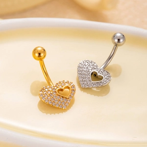 Macro shot of gold and silver heart belly rings with zircon stones in a ceramic dish