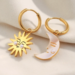 Macro shot of asymmetric 18K gold sun and moon hoop earrings with pearls on beige fabric
