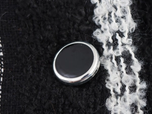 Macro view of a black round button with silver trim on a textured boucle knit coat