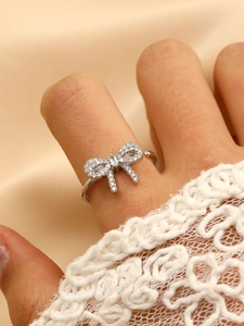 Detail of silver bow ring with shimmering zircon pave on champagne satin background