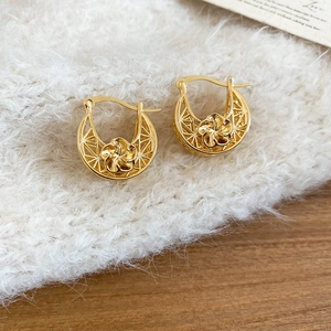 Detailed macro view of gold plated hollow flower earrings on a soft fabric and wood surface