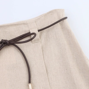 Dettaglio vita di gonna in lino beige con cintura sottile marrone e punte in metallo
