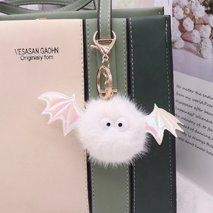 White faux mink fur bat keychain with holographic wings hanging on a beige handbag