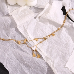 Detail of a 18K gold double-layer anklet featuring white shell heart tassels and beads