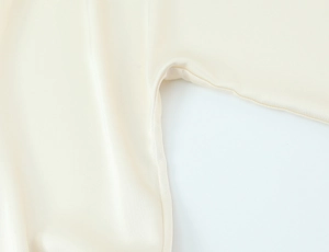 Detail of silk satin shirt showing sleeve seam stitching and cream fabric texture