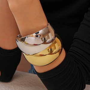 Detailed view of polished gold and silver irregular wide cuff bracelets on a wrist