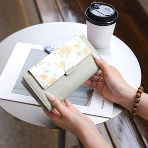 Detail of light green floral printed long wallet with golden buckle held by hands