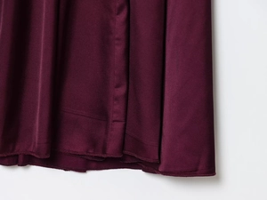 Dettaglio dell'orlo del vestito di raso bordeaux con cuciture e trama del tessuto
