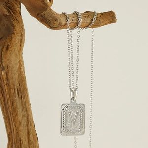 Minimalist silver stainless steel necklace with V-letter square pendant on a wooden branch