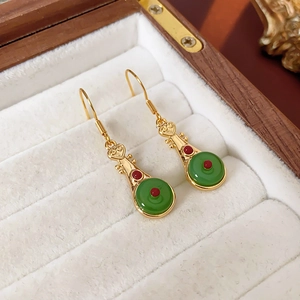 Detail of gold-plated lute earrings with green jade-like stones and red beads