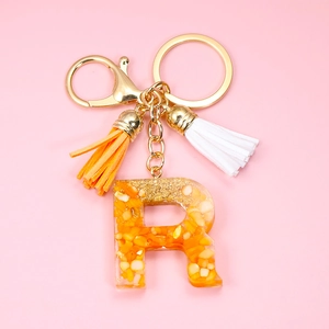 Detail of resin letter R keychain with orange stones, gold flakes and colorful tassels