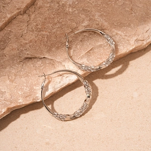 Detail of twisted silver hoop earrings with shimmering crystal pavé on stone surface